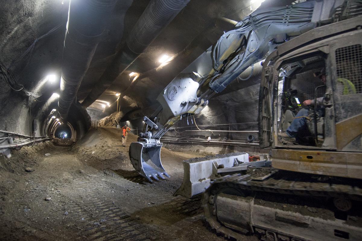 Construction crews excavate tunnel with heavy equipment and lighting underground.