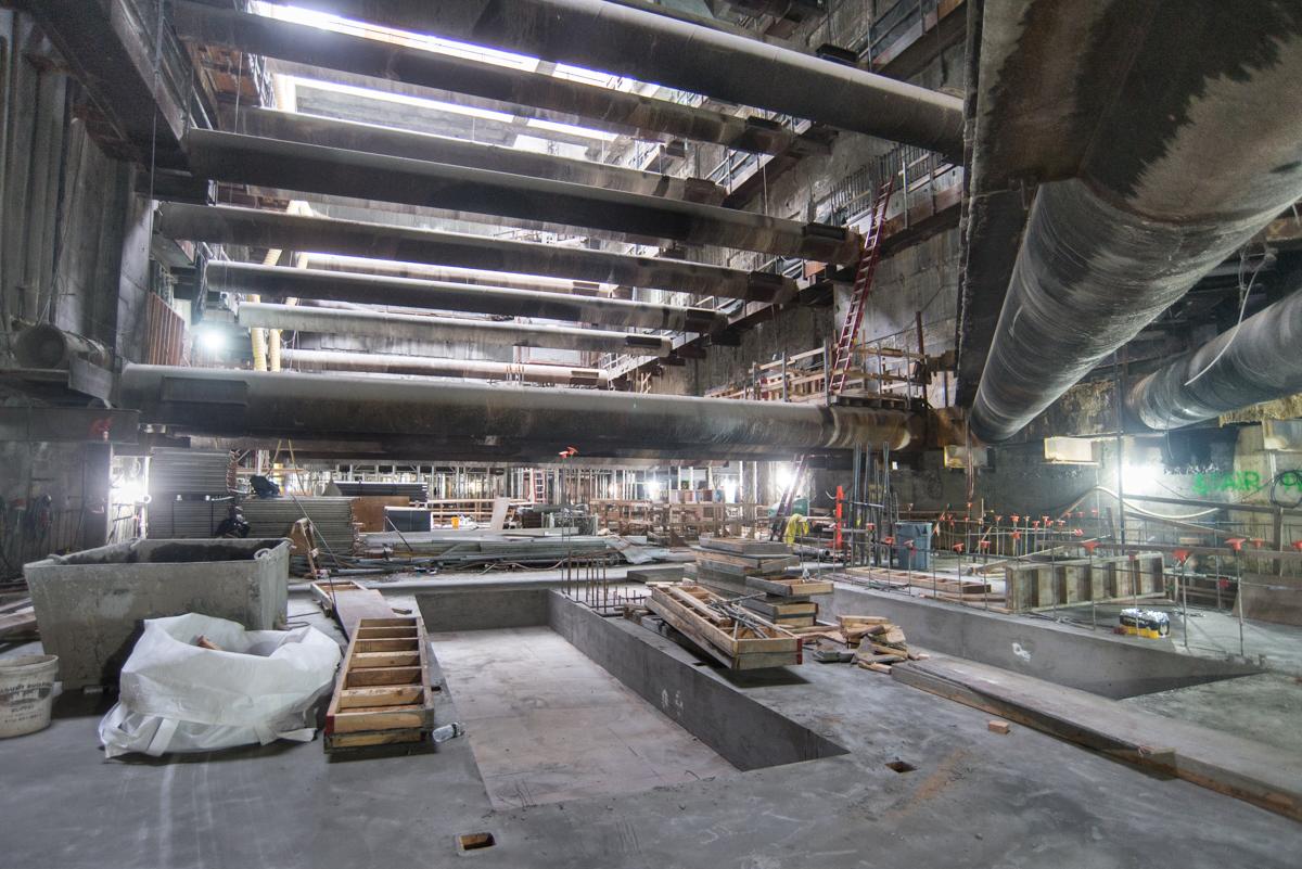 Construction site interior with concrete floor recesses, steel beams, and temporary lighting during transit station renovation.