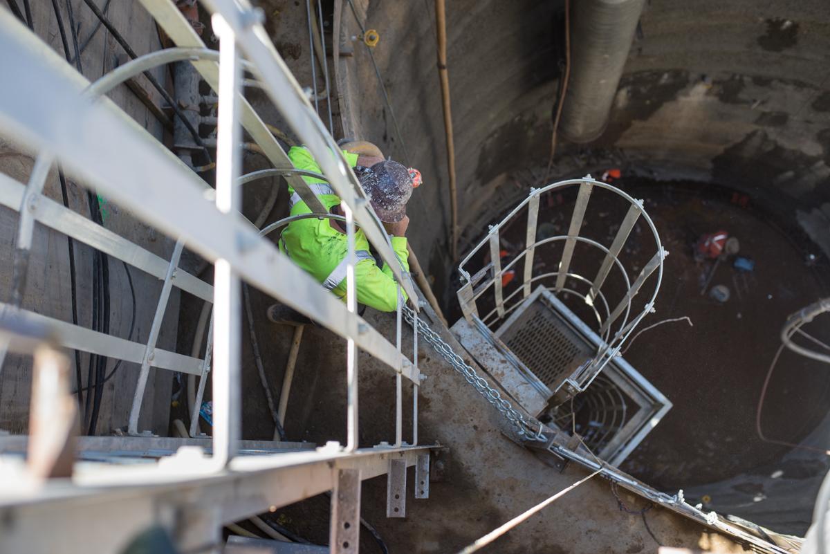 Construction worker in safety gear on wooden beam at underground shaft access point in Chinatown