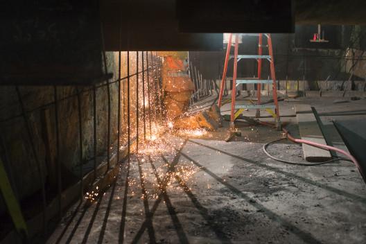 Construction site at transit station with metal ladder, steel framework, and excavation work visible under nighttime lighting.
