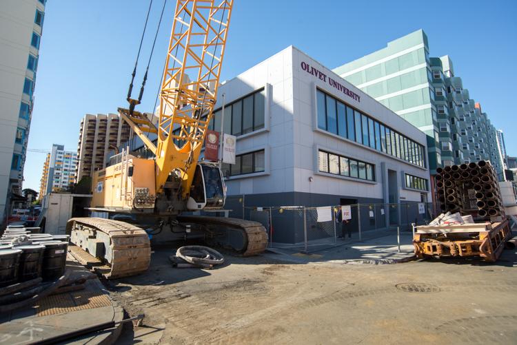 Construction crane and equipment on urban street with Olivet University building and surrounding high-rises