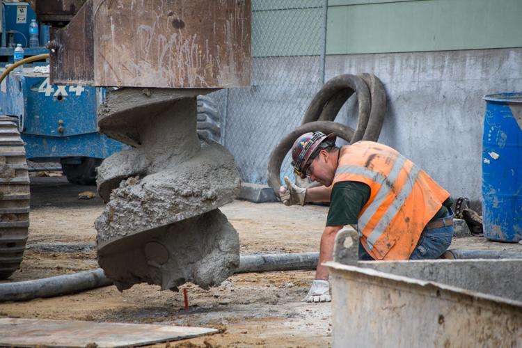 Worker in orange safety vest operating concrete mixer at construction site near Stockton Street station.