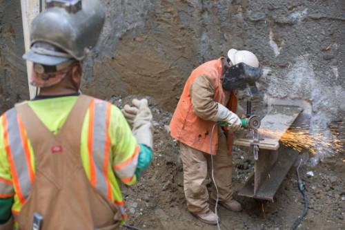 Worker using angle grinder on steel beam during underground transit station construction.