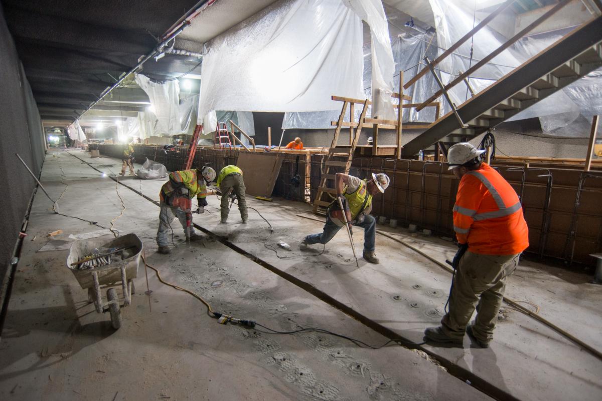 Workers in safety vests drill holes into concrete platform level for track plinth preparation work.