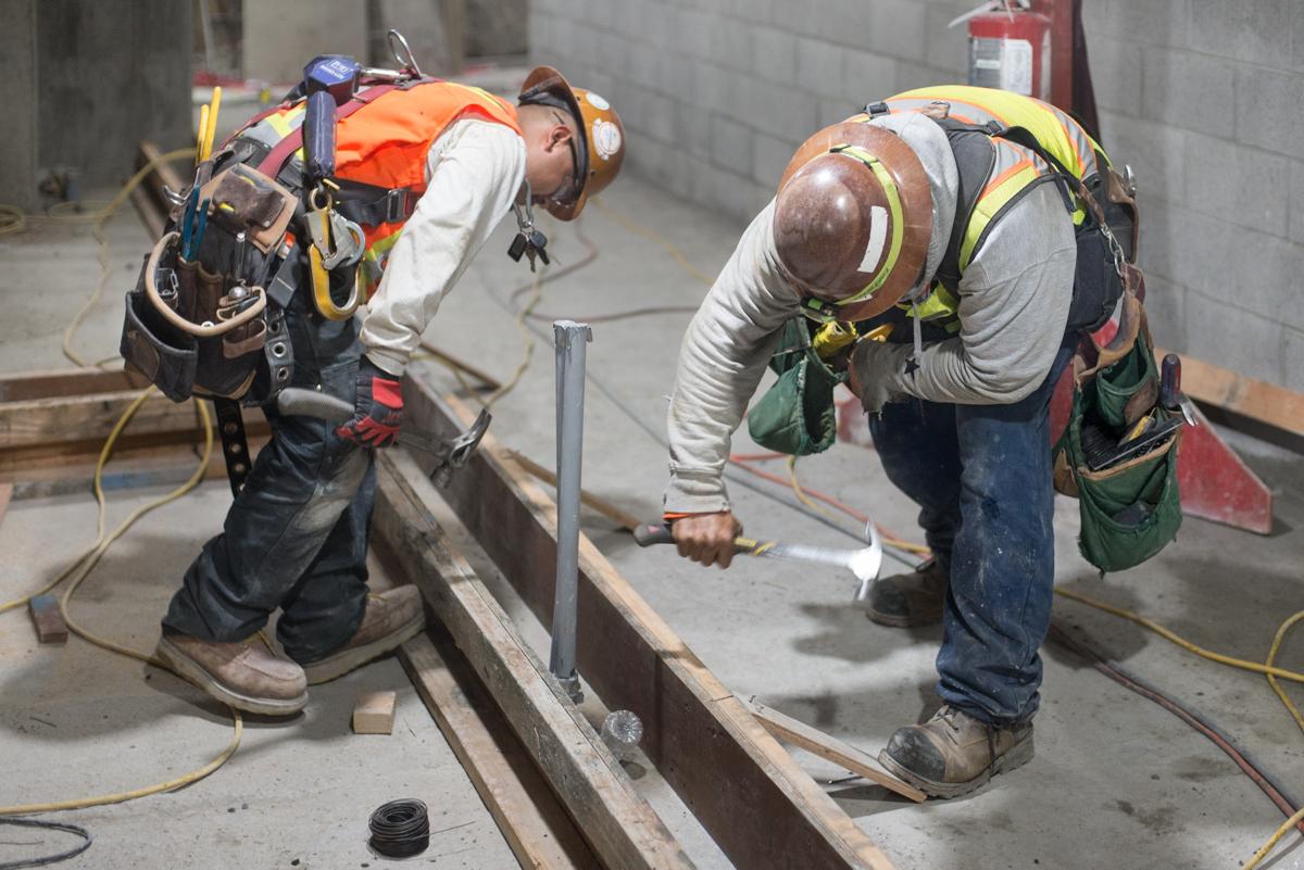 Two construction workers in safety gear install wooden formwork for concrete footing on a transit project.