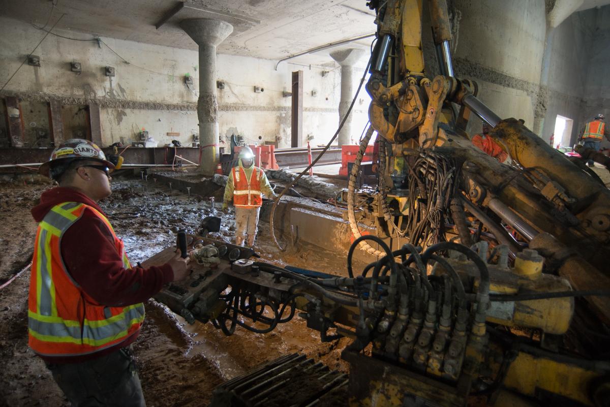 Workers operate drilling equipment in underground station excavation at Union Square.