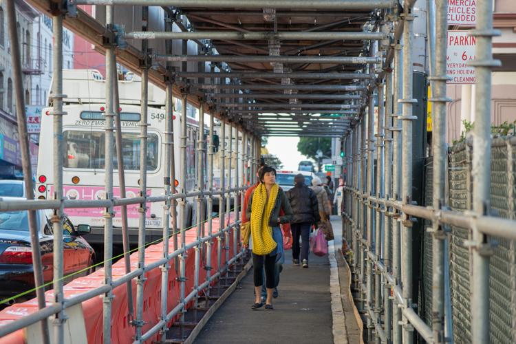 Covered pedestrian walkway with metal railings and overhead structure, people walking through, street visible on left side.