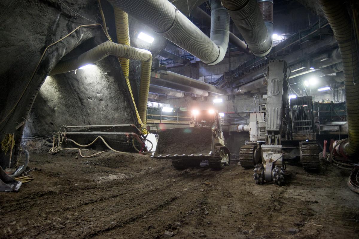 Underground construction site with bulldozer, excavation equipment, and ventilation ducts in cavern.