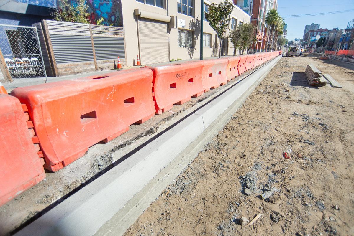 Red plastic barrier fencing along a concrete curb on a city street under construction.