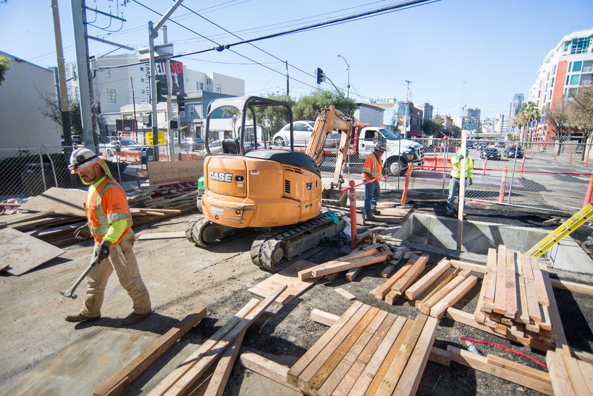 Construction workers operate excavator and remove wooden forms at 4th and Townsend street construction site.
