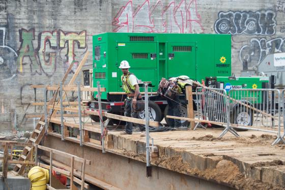 Workers in hard hats construct safety fencing at Chinatown Station headhouse construction site.