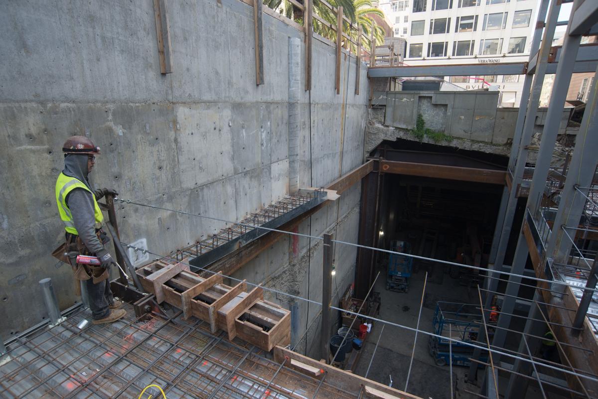Construction worker in safety gear installing rebar on steel deck for underground transit station platform.