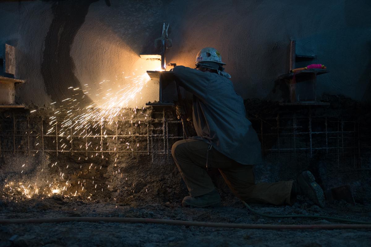 Worker welding metal framework in underground transit station construction area with bright sparks flying.