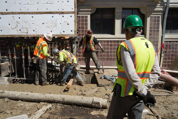 Construction workers lower a steel rebar cage for underground station wall reinforcement at Chinatown Station.