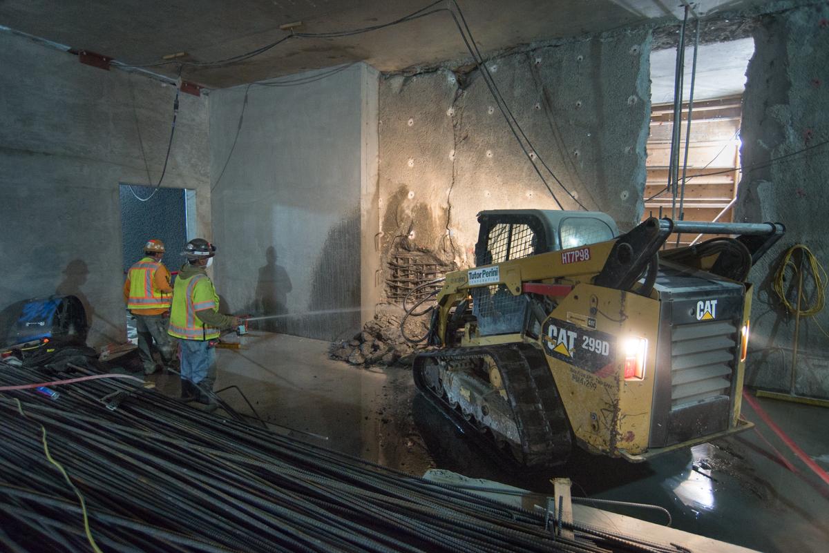 Workers spray water during underground demolition and construction using a CAT skid steer loader in a concrete tunnel.