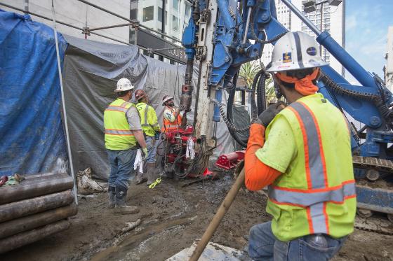 Construction workers in safety vests operate drilling equipment at Stockton Street and Geary Boulevard.