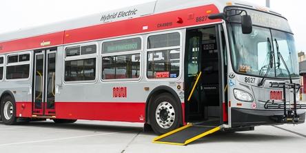 Red and white New Flyer hybrid bus with deployed wheelchair ramp and yellow safety edge.