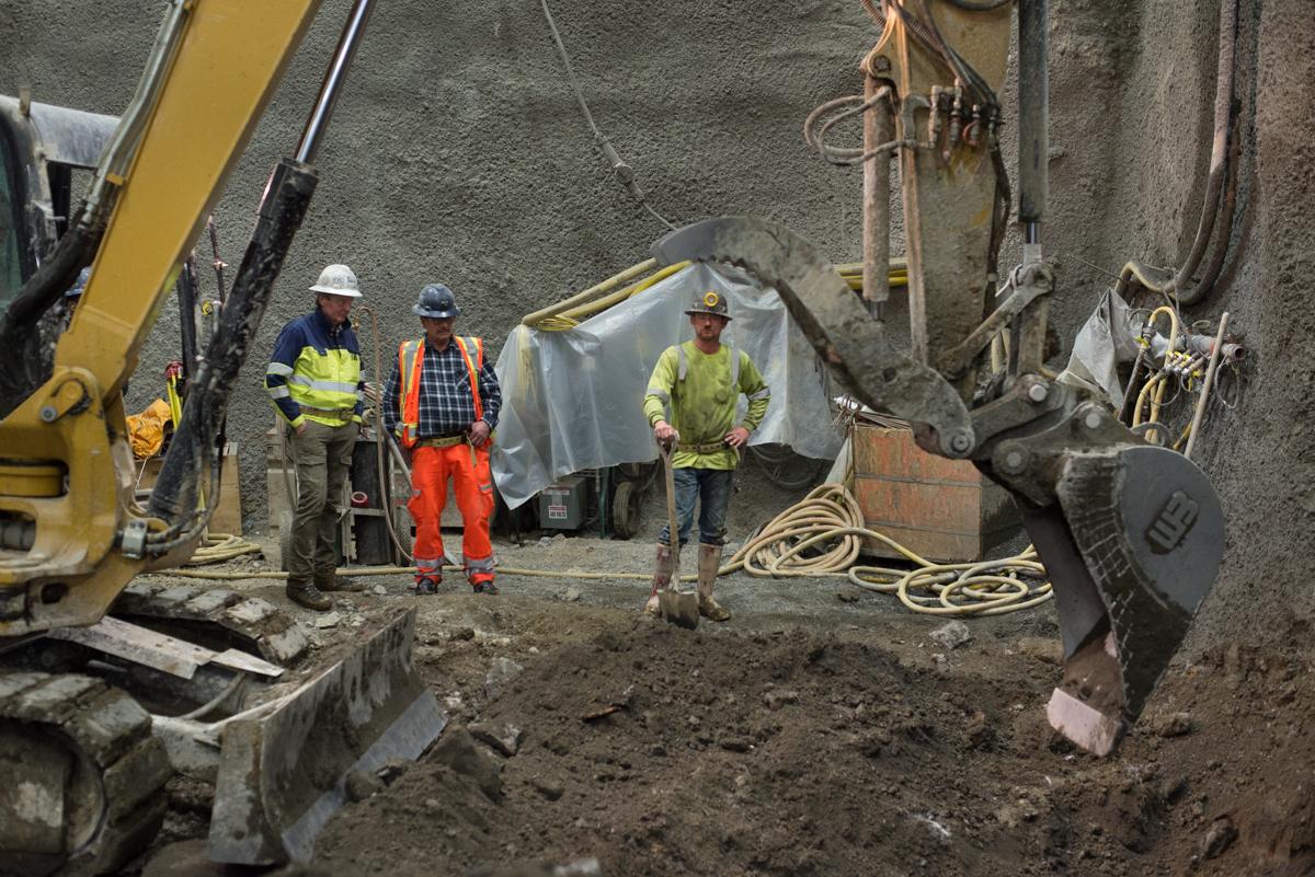 Construction workers monitor excavation equipment operating in an underground tunnel cavern during platform construction.