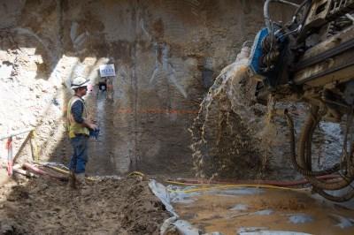 Worker removes drill shaft as water sprays from dewatering well installation on Stockton Street.