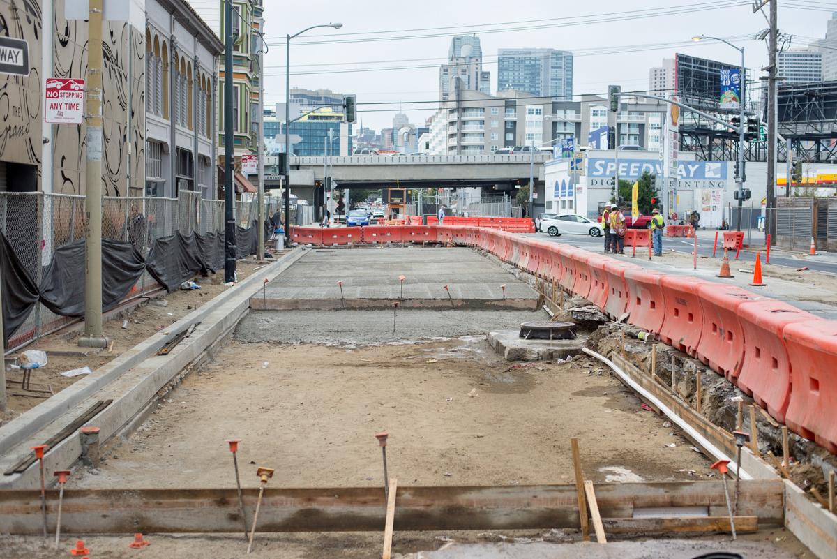 Construction site on 4th Street with excavated area, red barriers, and city skyline in background.