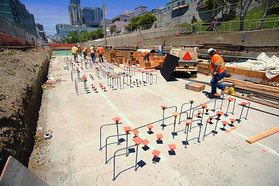 Construction site with concrete foundation work, rebar framework, and workers in safety gear on 4th Street.