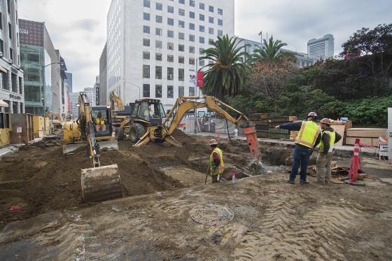 Construction crew operating excavators and heavy equipment on Stockton Street, with workers in safety vests on an active dig site.