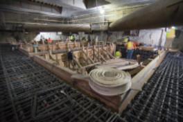 Workers construct reinforcement cage and concrete forms inside underground transit station box.