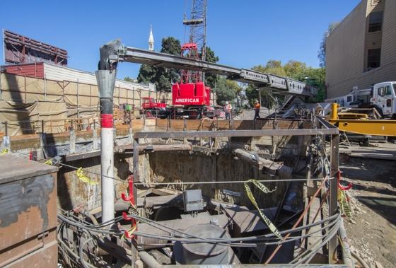 Construction equipment and workers at an underground retrieval shaft site in North Beach with street barriers and fencing.