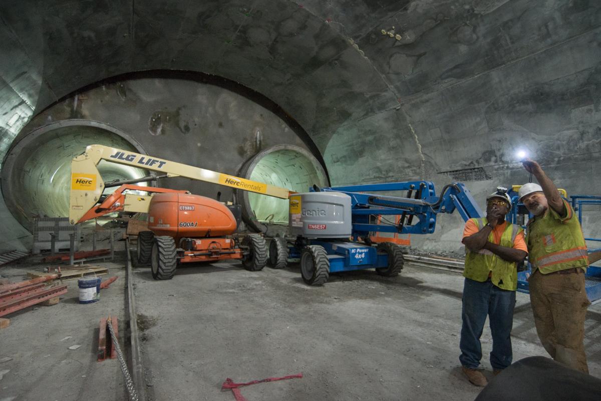 Workers inspect construction equipment inside a large underground tunnel cavity during Central Subway construction.