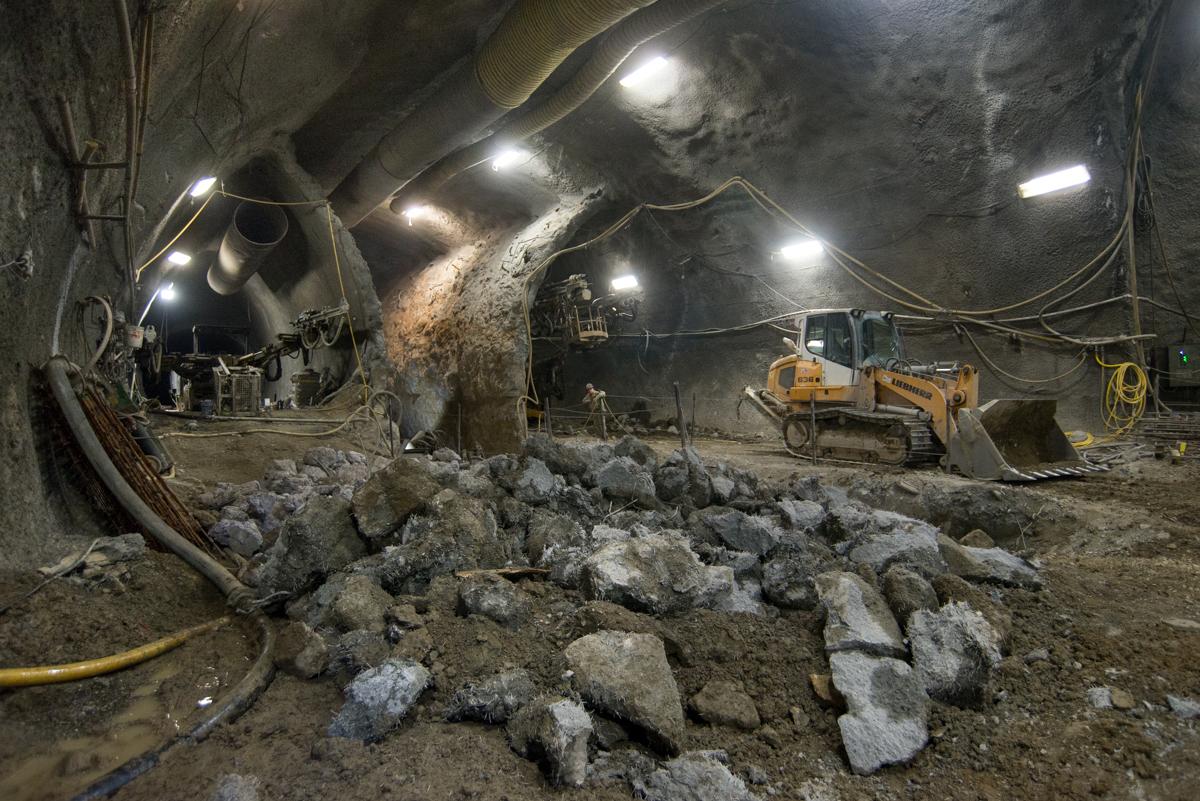 Underground tunnel with construction equipment and workers removing concrete debris from platform cavern