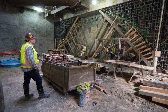 Construction worker in safety gear observing wooden formwork and rebar framework for Chinatown Station underground entrance.