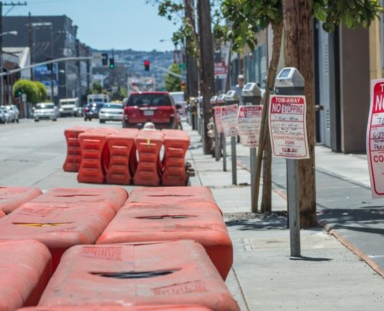 Red plastic barriers line a city sidewalk during utility work on Brannan Street.