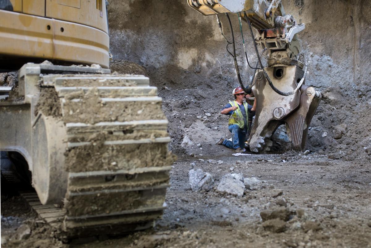 Worker in safety gear operates large mechanical claw for excavation work at construction site.
