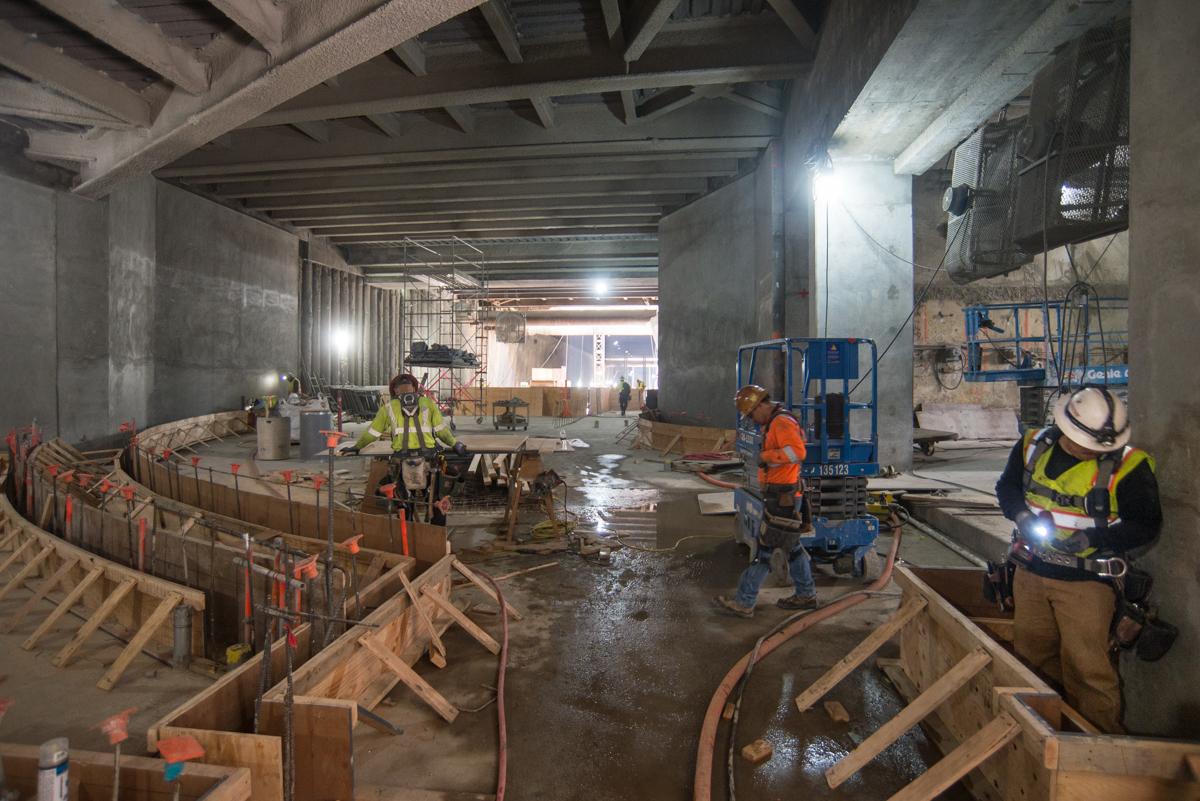Construction workers install concrete forms for wall footings in underground transit station concourse.
