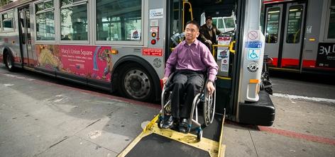 Person in wheelchair using yellow ramp to exit bus at street level