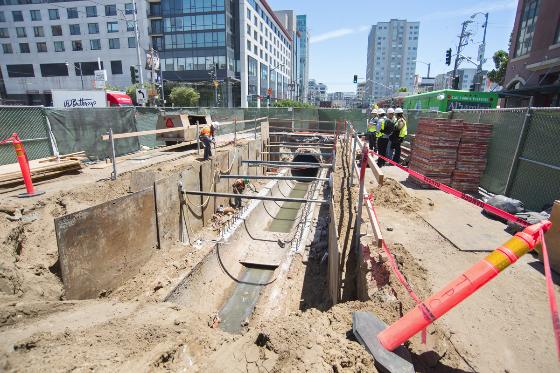Construction site showing excavated underground tunnel with reinforced concrete structure and safety barriers in urban setting.