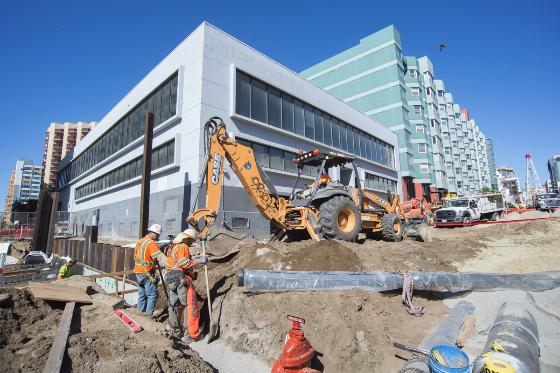 Construction workers and equipment excavating foundation with rebar for Yerba Buena/Moscone Station, downtown buildings visible.