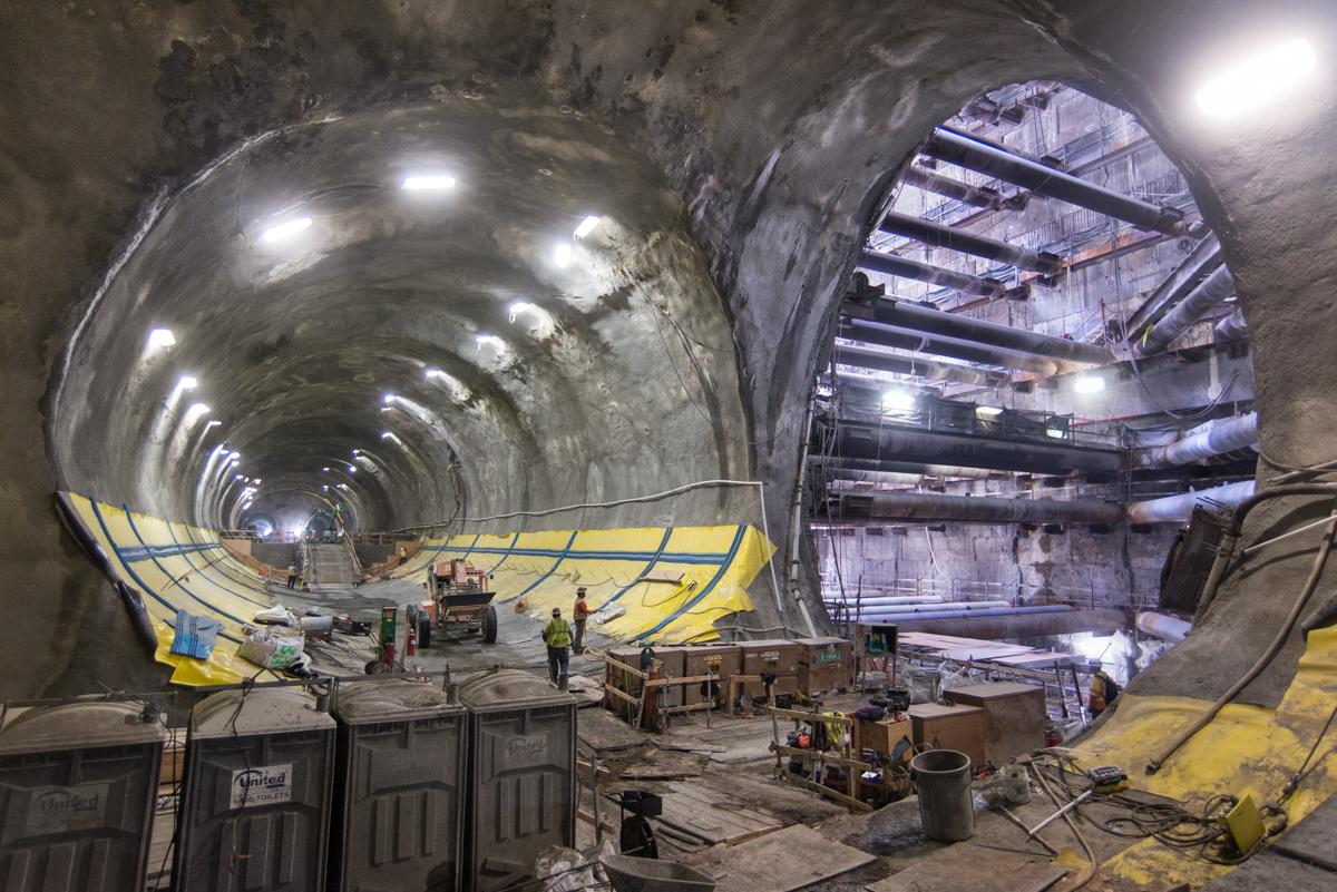 Construction workers inside a large concrete tunnel with yellow safety markings and industrial lighting during Central Subway construction.