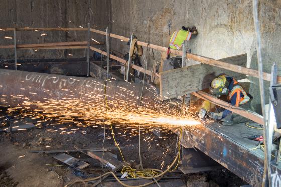 Workers cutting steel plate with sparks flying at Chinatown Station construction site.