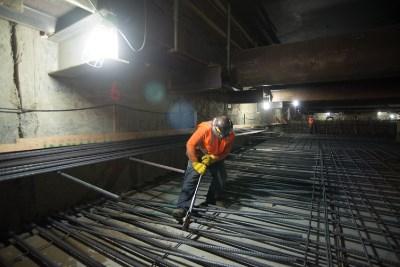 Worker in orange safety gear tightening rebar with wrench on construction site floor.