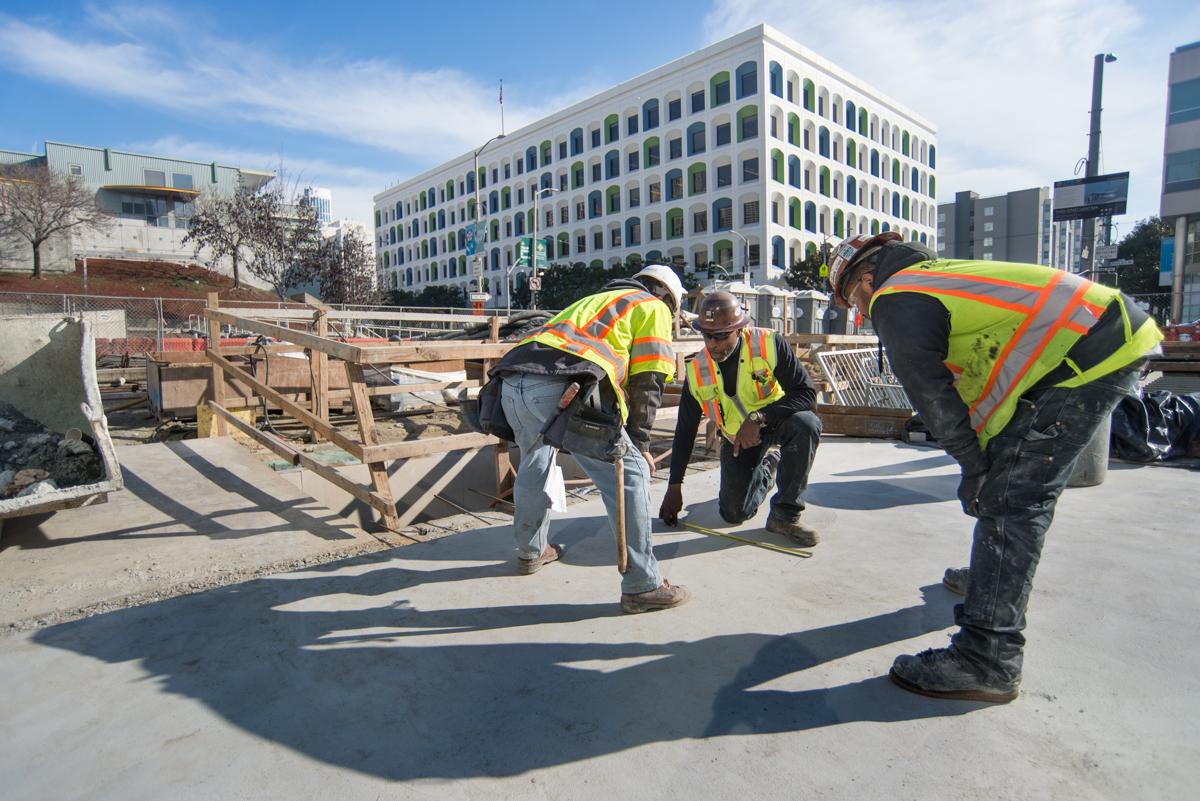 Construction workers in safety vests work on concrete platform at transit station construction site.