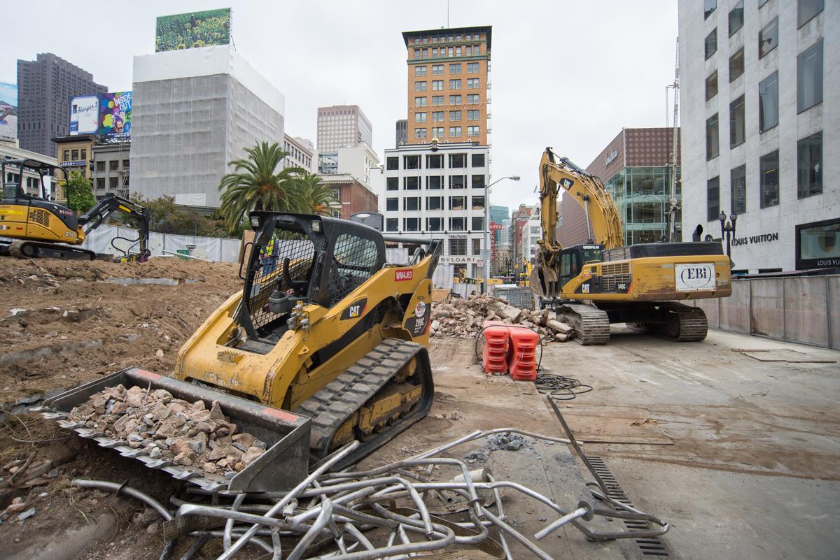 Construction equipment and debris removal at urban demolition site with yellow excavator and skid loader.