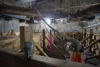 Underground construction site with wooden support structures, concrete floor, metal pipes, and temporary ventilation shaft.