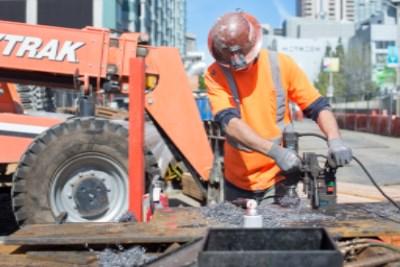 Worker in safety gear operating concrete saw on 4th Street construction site.