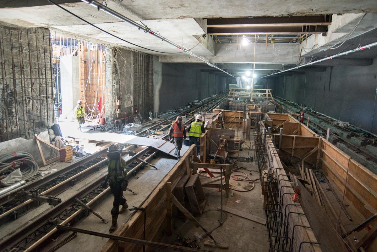 Workers in safety vests construct underground station platform foundations in a concrete tunnel.