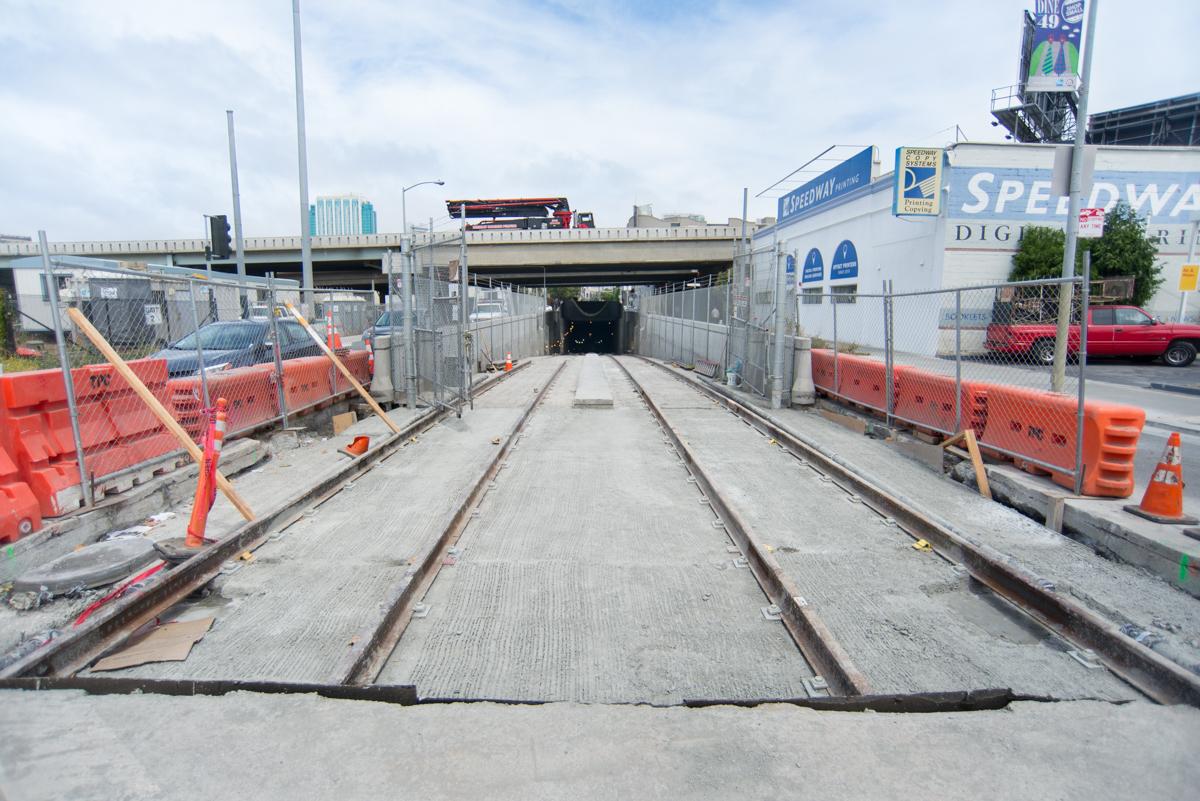 Construction site showing new streetcar track sections at tunnel entrance with safety barriers and equipment.