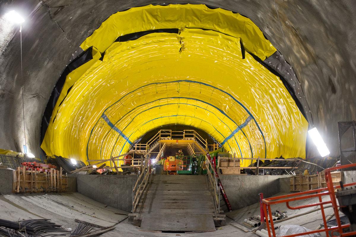 Yellow-draped tunnel interior with construction equipment and metal framework during Chinatown Station headhouse construction.