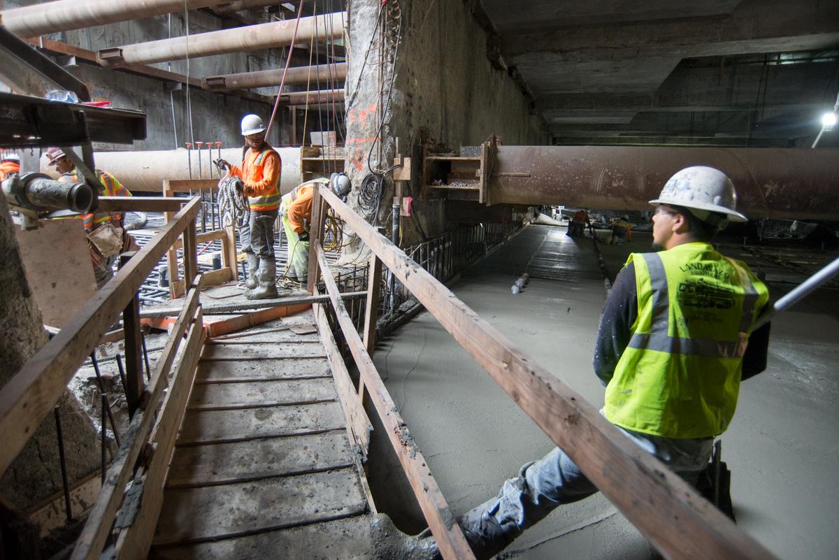 Construction workers in safety gear smooth concrete on the Central Subway tunnel floor slab.