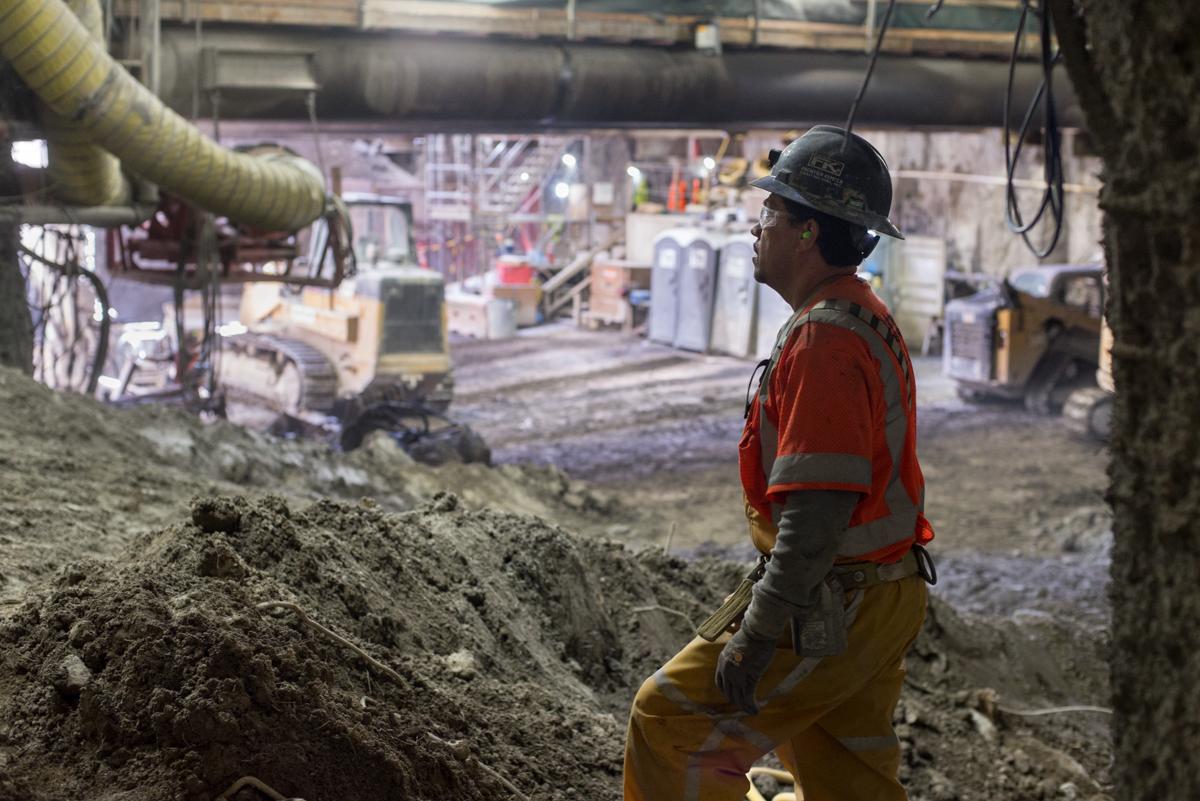Worker in hard hat and safety vest observing underground excavation work in transit tunnel construction site.