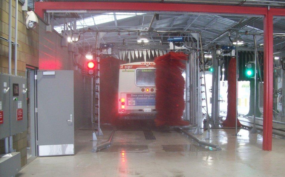 Red traffic signal illuminated above automated train wash station with red metal frame structure.